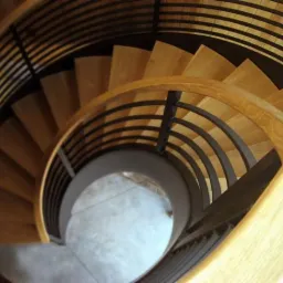 Spiralne schody z jasnego drewna i czarnymi metalowymi balustradami, widziane z góry, ukazujące elegancki design i precyzję wykonania.