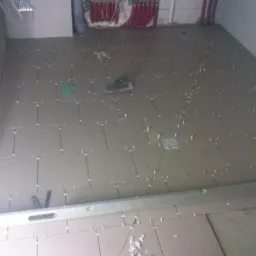 Układanie szarych płytek podłogowych w łazience, widoczny poziomica, krzyżyki dystansowe i odpływ liniowy w posadzce, na ścianie instalacja CO z czerwonymi rurami.