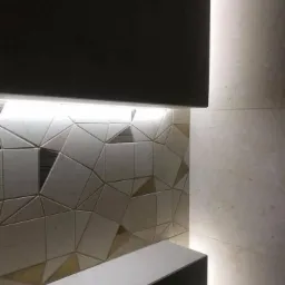 Fragment ściany łazienki z geometryczną mozaiką i podświetleniem LED, widoczny fragment blatu umywalki.