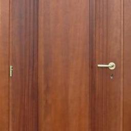 Mp Drzwi - Klasyczne, brązowe drzwi wewnętrzne z dekoracyjnymi frezowaniami i złotą klamką, widoczne zawiasy. Drzwi w stylu retro.