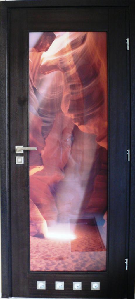 Ciemne drzwi wewnętrzne z szybą z motywem kanionu w Radomyślu nad Sanem. Szyba z grafiką, srebrna klamka, cztery małe, kwadratowe dekoracje na dole.