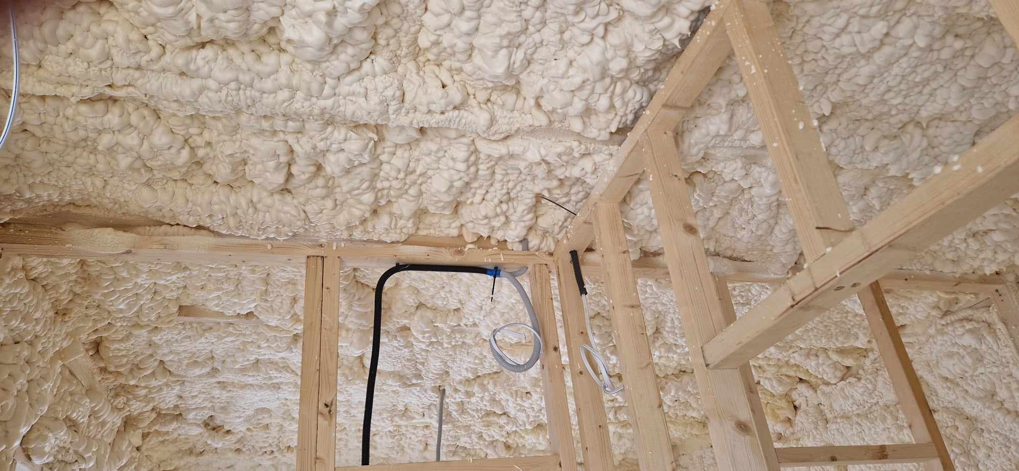 Wnętrze w trakcie izolacji pianą poliuretanową, widoczne drewniane elementy konstrukcyjne i instalacje elektryczne.
