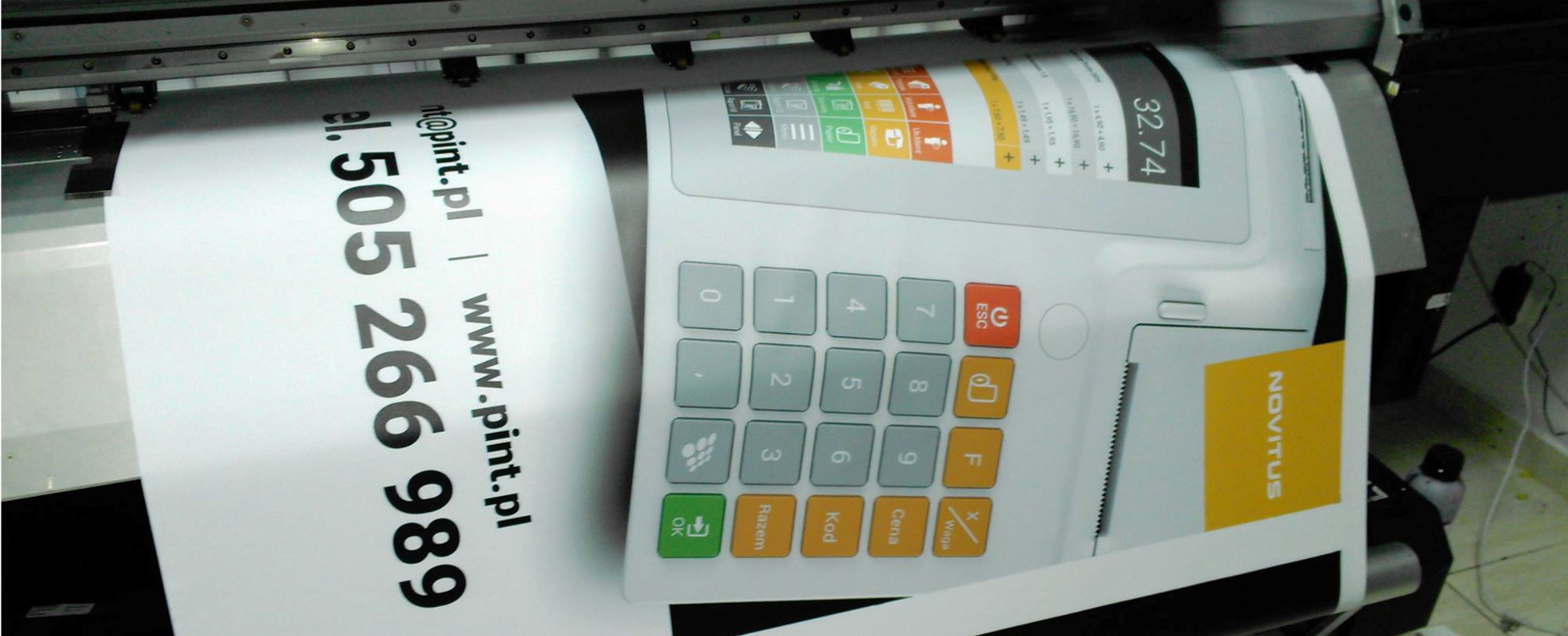 Druk wielkoformatowy plakatu z wizerunkiem kasy fiskalnej Novitus, widoczne numery telefonu i adres strony internetowej drukarni.