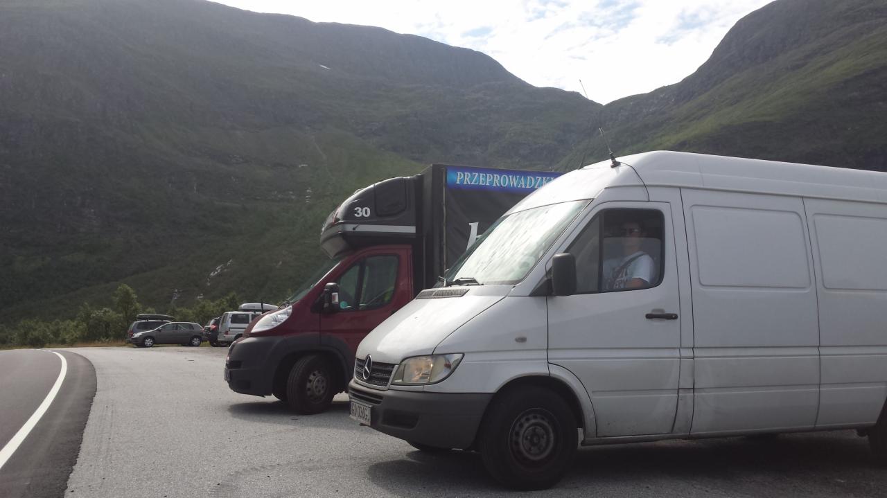 Dwa busy na tle górskiego krajobrazu, jeden z napisem 'Przeprowadzki', drugi czerwony z numerem '30'. Biały bus z kierowcą w kabinie na pierwszym planie.
