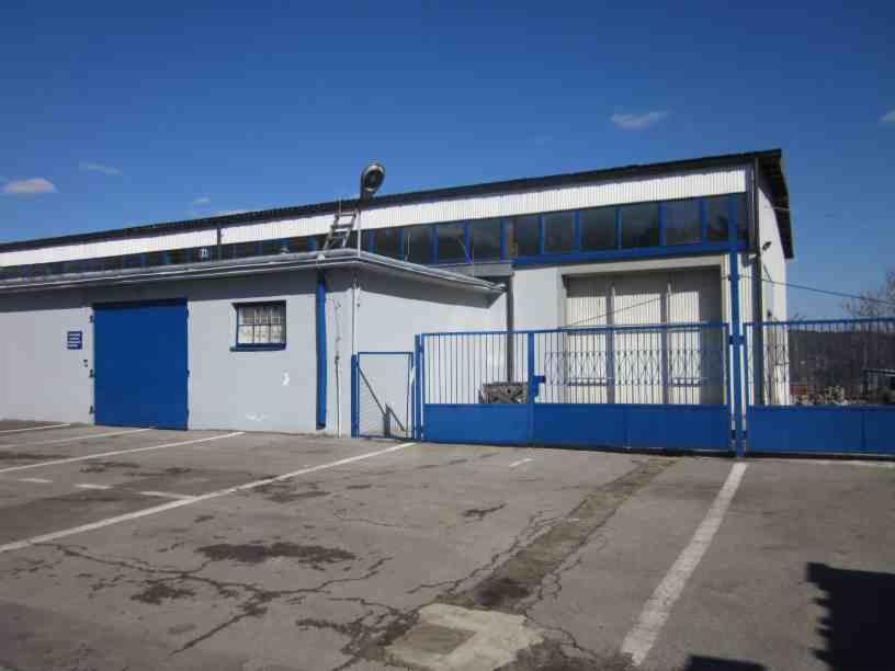 Zewnętrzny widok hali magazynowej z niebieską bramą, ogrodzeniem i rampą załadunkową na tle błękitnego nieba.