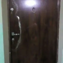 Brązowe drzwi wejściowe z wizjerem i zamkiem, zabezpieczone folią ochronną, w trakcie montażu.