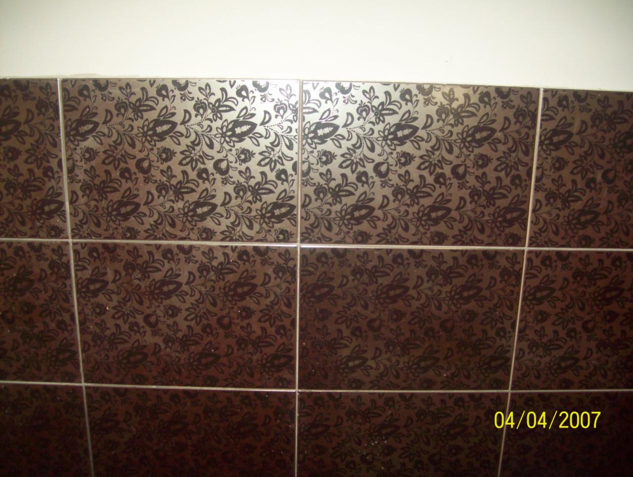 Brązowe, kwadratowe płytki z motywem kwiatowym, ułożone na ścianie. Biała fuga. Widoczny fragment białej ściany nad płytkami. Data w prawym dolnym rogu: 04/04/2007.