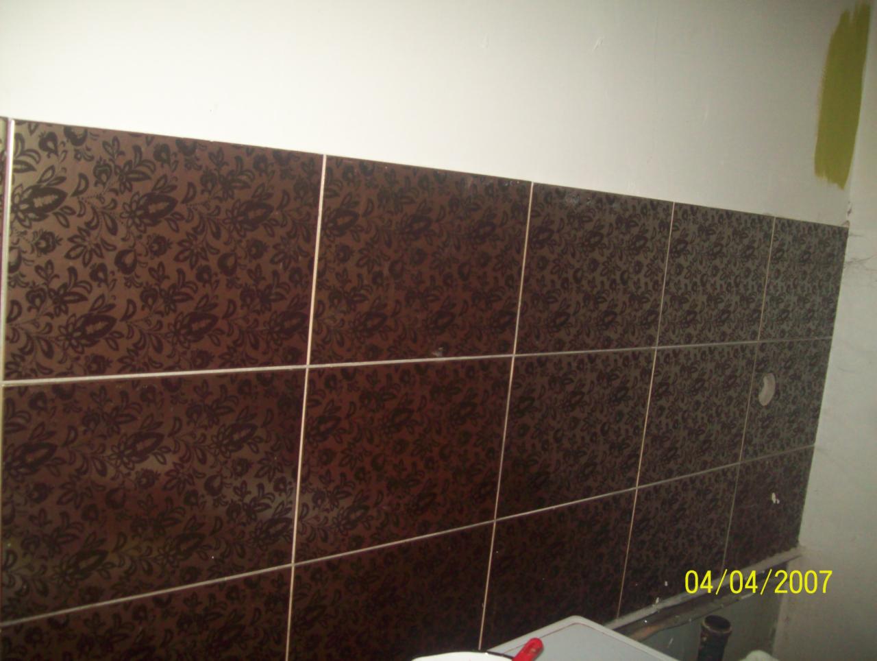 Ułożone brązowe płytki ceramiczne z motywem kwiatowym na ścianie nad umywalką. Widoczne fugi i fragment ściany pomalowanej na biało. Data na zdjęciu: 04/04/2007.