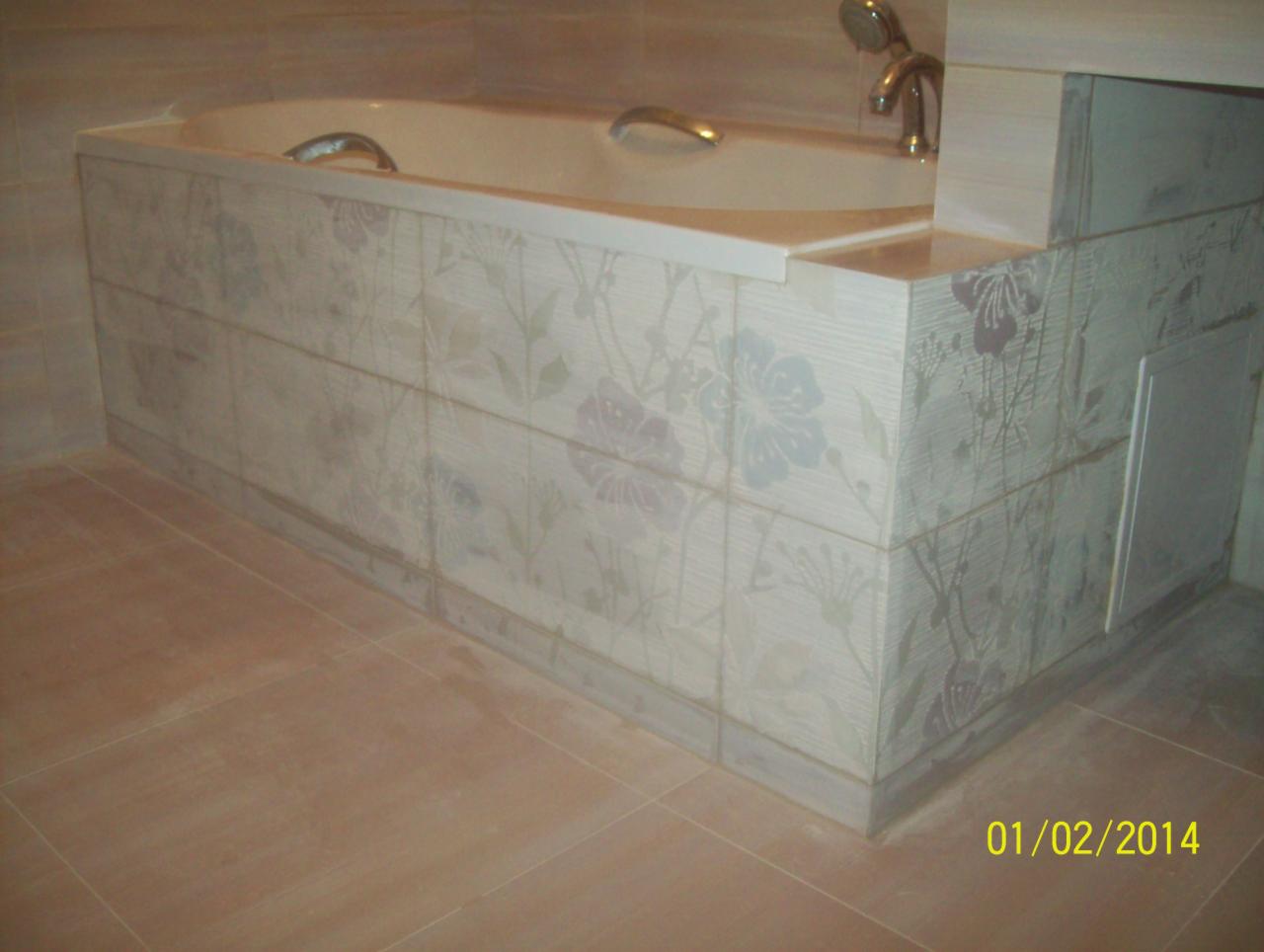 Wykończona obudowa wanny z płytek ceramicznych z motywem kwiatowym, dopasowana do podłogi. Widoczna armatura i fragment kabiny prysznicowej. Estetyczne połączenie kolorów.