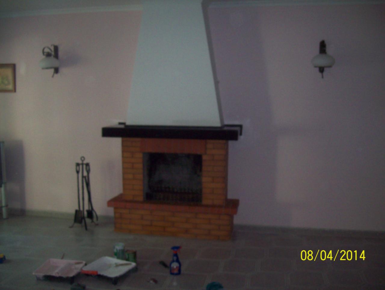 Pokój z murowanym kominkiem przed malowaniem ścian. Widoczne akcesoria malarskie: kuwety i pędzle. Na ścianach zamontowane kinkiety. Ujęcie z perspektywy podłogi.