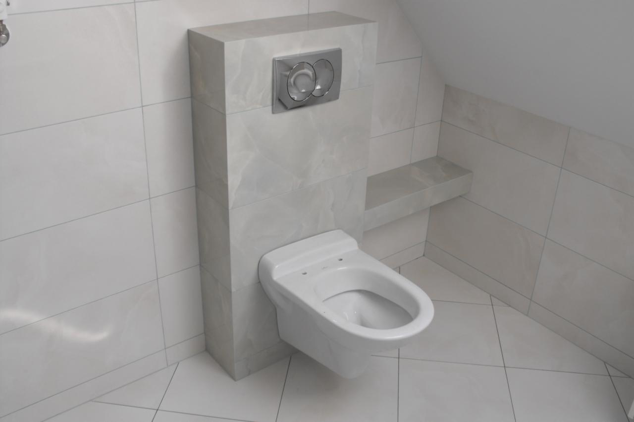 Podwieszana toaleta w łazience na poddaszu, wykończona płytkami imitującymi marmur, z chromowanym przyciskiem spłukującym i półką wnękową.