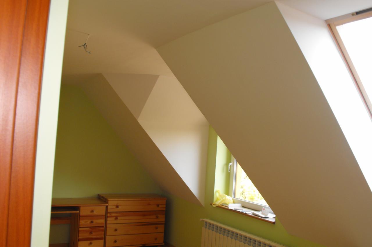 Poddasze po remoncie: skośne ściany pomalowane na kremowo, okno dachowe, drewniane meble. Widoczne gładzie i świeże malowanie, podkreślające geometrię przestrzeni.