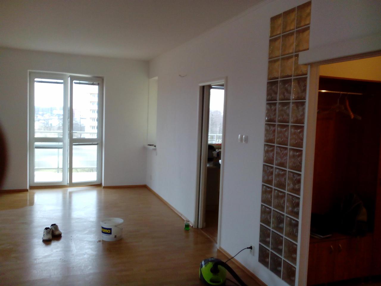 Jasne wnętrze po remoncie: świeżo pomalowane ściany, parkiet, okno balkonowe, dekoracyjny panel z luksferów, odkurzacz i wiadro z farbą na podłodze.