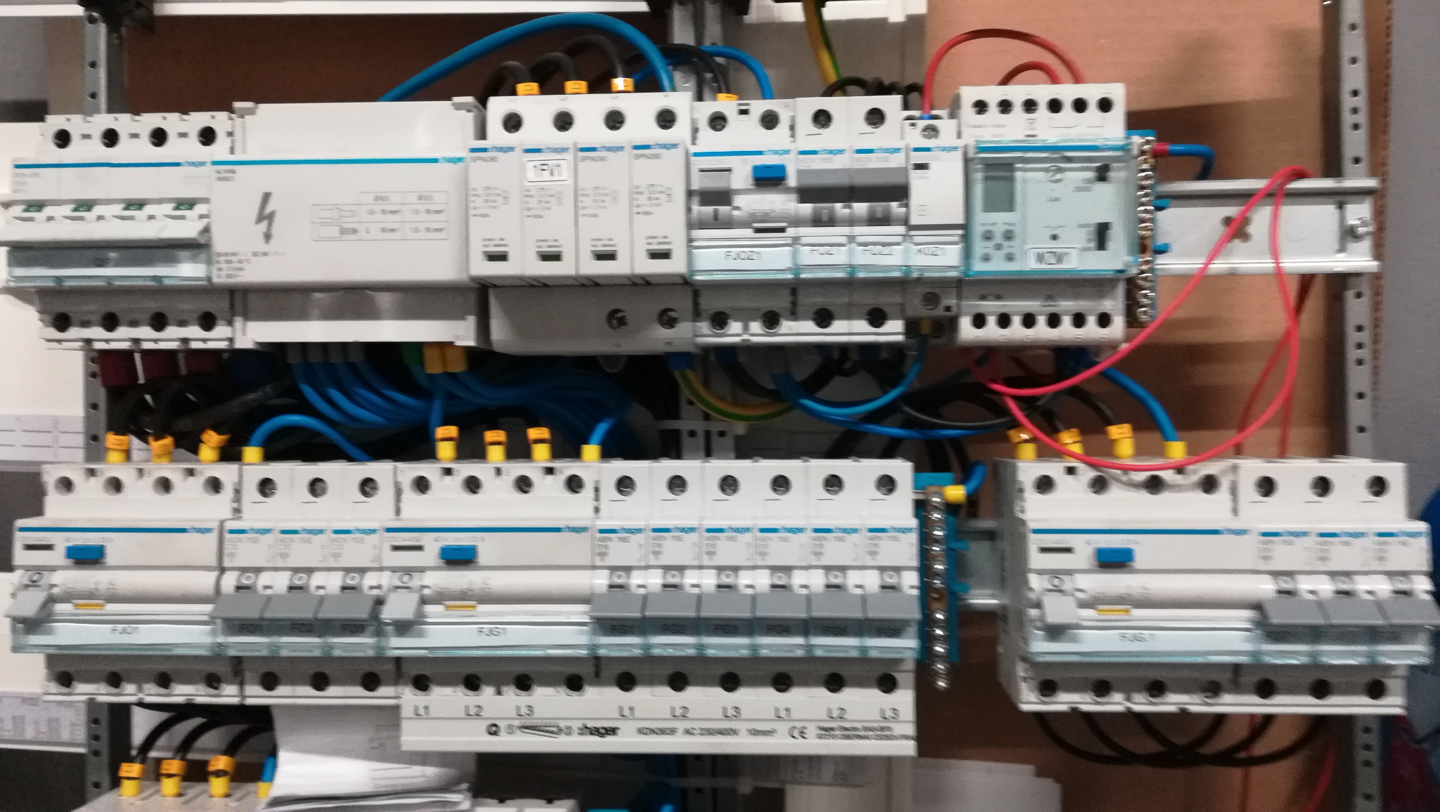 Rozdzielnia elektryczna z zainstalowanymi bezpiecznikami, przewodami w kolorach niebieskim, czarnym i czerwonym, zamontowana na metalowej szynie wewnątrz szafy sterowniczej.