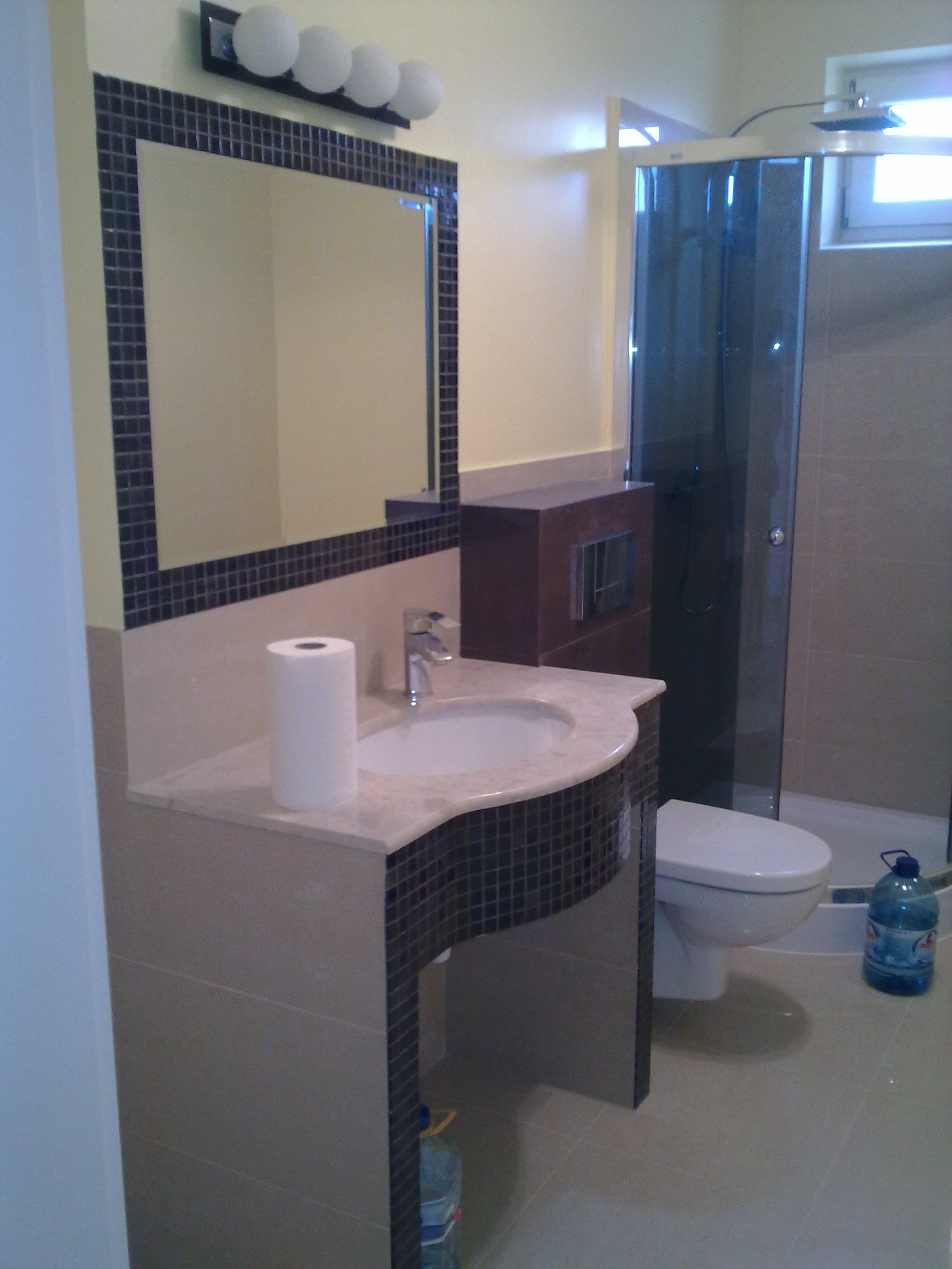 Wykończona łazienka w Dębicy: umywalka z mozaiką, lustro z oświetleniem i kabina prysznicowa. Jasne płytki i minimalistyczny design.