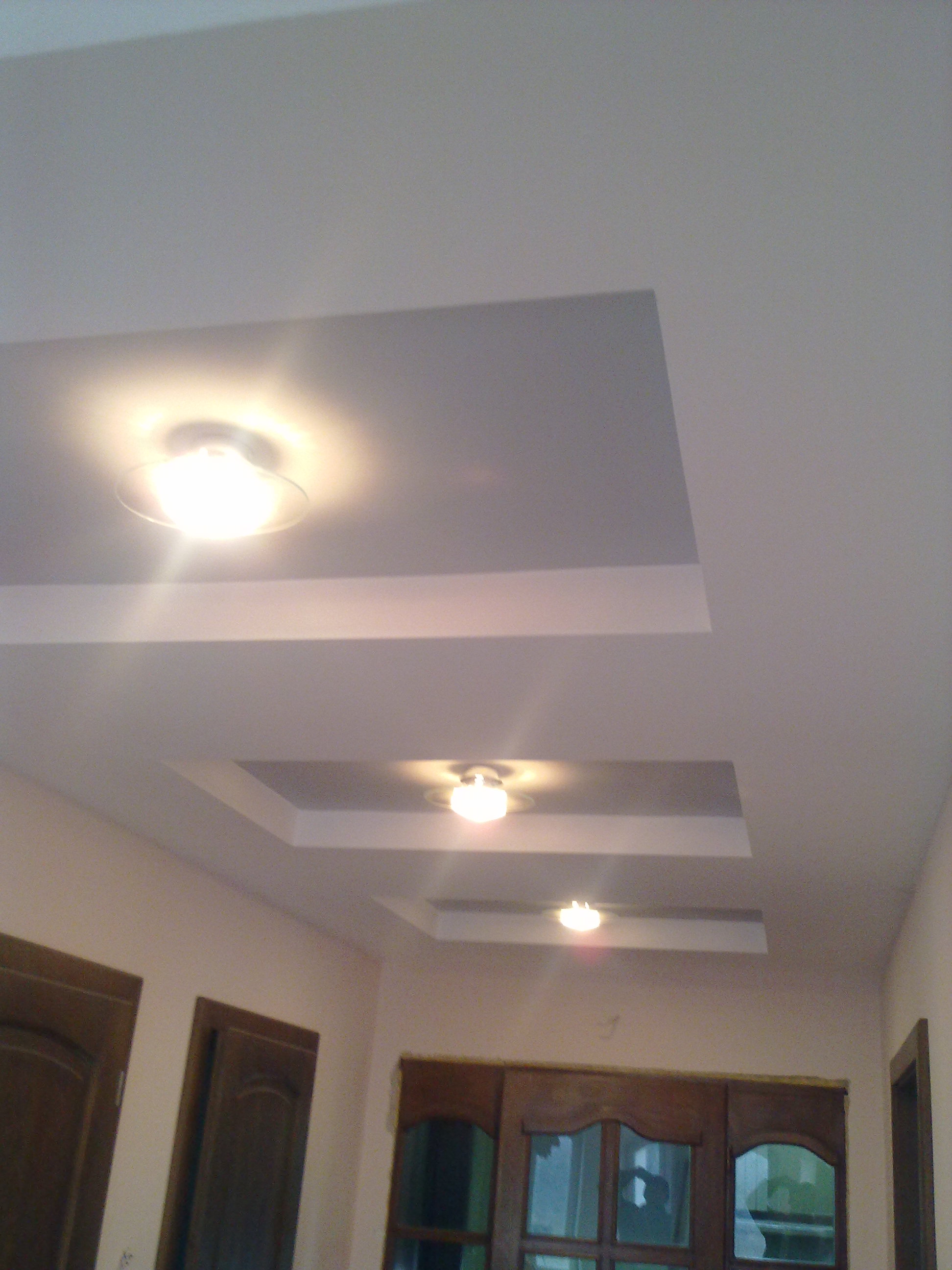 Wykończony sufit podwieszany z oświetleniem punktowym w salonie. Widoczne trzy kwadratowe wnęki z zamontowanymi lampami. Ściany w jasnym odcieniu.