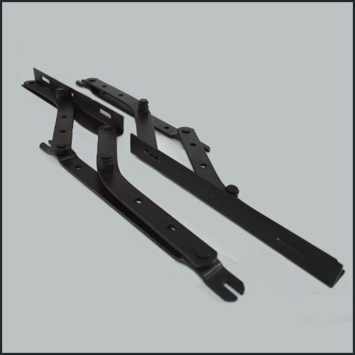Dwa czarne, metalowe zawiasy okienne, leżące ukośnie na szarym tle. Widoczne otwory i mocowania.