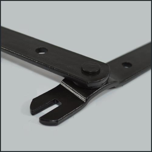 Czarny, metalowy zawias z charakterystycznym wycięciem, sfotografowany w zbliżeniu na gładkim, szarym tle. Widoczne detale łączenia i otwory montażowe.