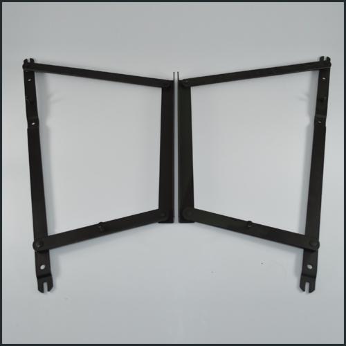 Dwa czarne, metalowe mechanizmy podnoszenia, prawdopodobnie do mebli, ułożone symetrycznie na jasnym tle. Widoczne nity i otwory montażowe.