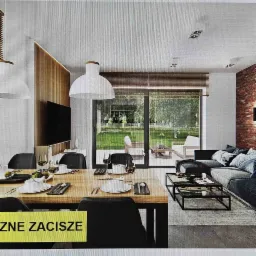 Jasne, przestronne wnętrze domu z dużym oknem na ogród, drewnianą ścianą z telewizorem i ceglaną ścianą, stół z nakryciem i sofa z poduszkami.