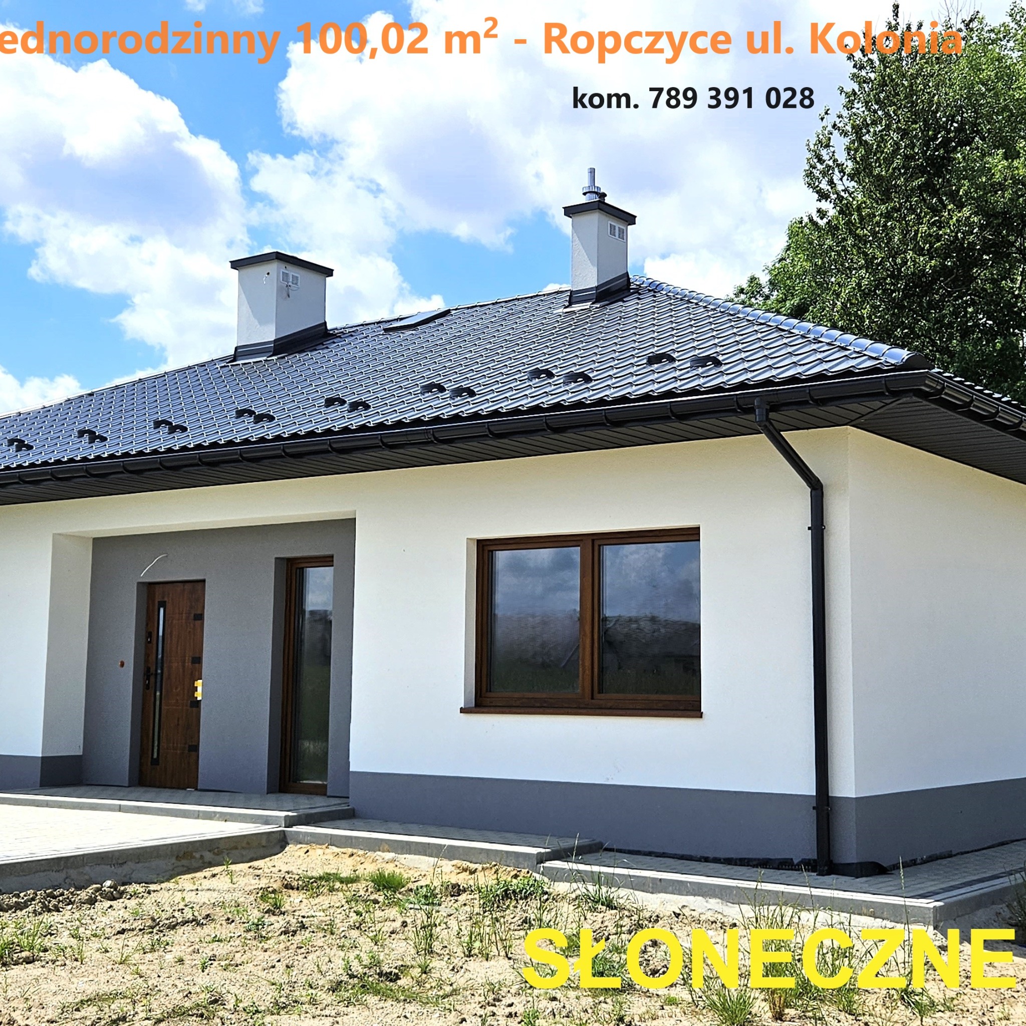 Nowoczesny, parterowy dom jednorodzinny z ciemną dachówką i czarnymi rynnami, widoczne dwa kominy, brązowe okna i drzwi wejściowe, teren wokół domu częściowo zagospodarowany, błękitne niebo...