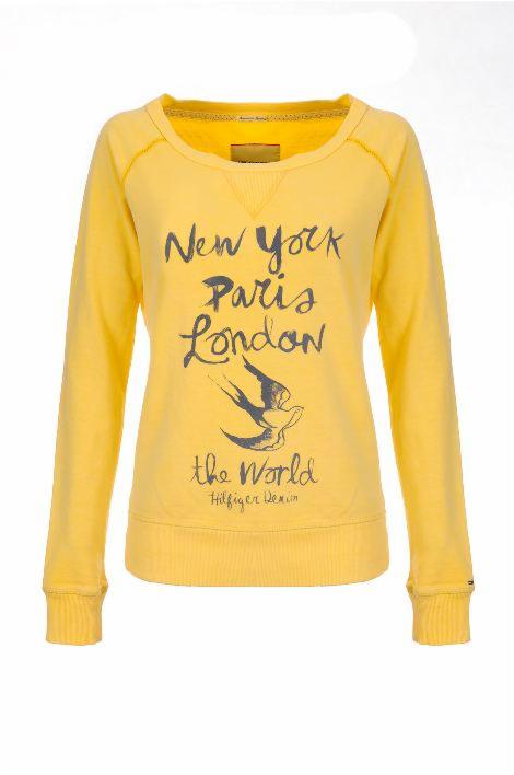 Żółta bluza damska z długim rękawem, nadrukiem 'New York Paris London the World' i motywem jaskółki, na białym tle. Raglanowe rękawy.