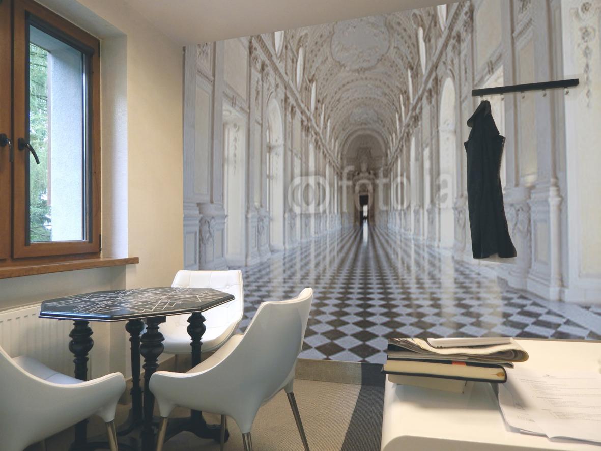 Pokój z fototapetą imitującą pałacowy korytarz. Na pierwszym planie stół z krzesłami i dokumenty. Czarna szata wisi na wieszaku.