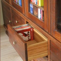 Stolarstwo - Jakub Trojanowski - Dębowa biblioteczka z przeszklonymi półkami i wysuwaną szufladą wypełnioną płytami CD, widoczny detal wykonania szuflady z jasnego drewna.