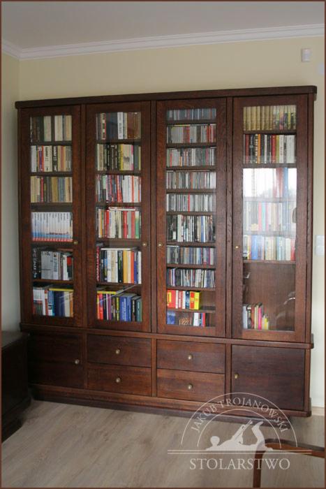 Dębowa biblioteczka z przeszklonymi drzwiczkami, wypełniona książkami i płytami CD, z rzędem szuflad w dolnej części.