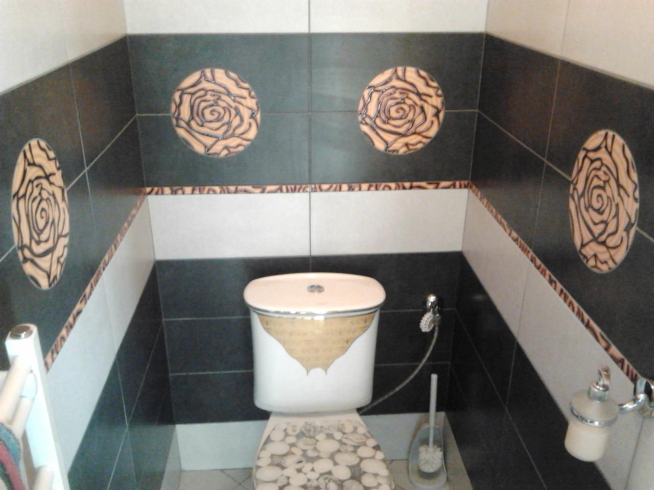 Wykończona toaleta z czarno-białymi płytkami i dekoracyjnymi rozetami. Uwagę zwraca wzór na desce sedesowej imitujący kamienie.