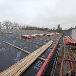 ANETA STEFANIAK SEBA-DACHY USŁUGI CIESIELSKO DEKARSKO BUDOWLANE - Dach pokryty membraną Budmat, z łatami i kontrłatami przygotowany do dalszych prac dekarskich. Widoczne drewno konstrukcyjne i rusztowanie. Pochmurne niebo w tle.