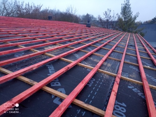 Czerwone łaty na czarnej membranie dachowej, widok z góry. Konstrukcja dachu w trakcie budowy, z widocznymi elementami drewnianymi i membraną izolacyjną.