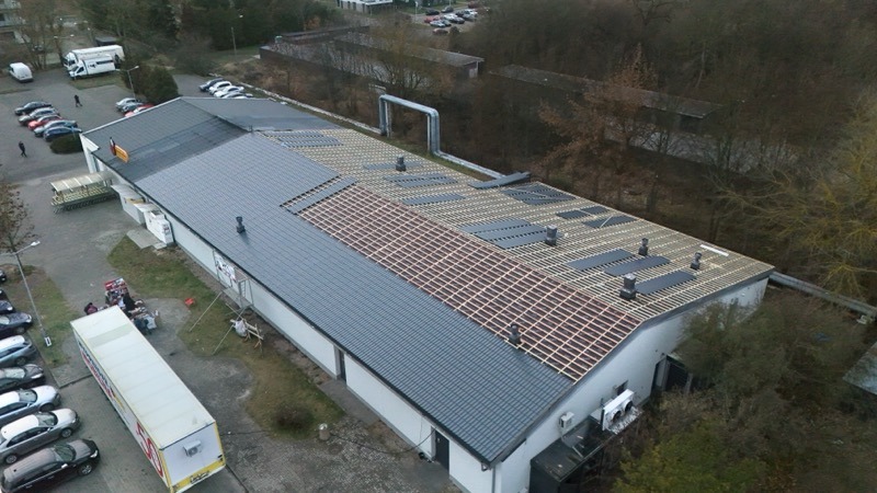 Widok z góry na budynek z częściowo wymienionym dachem. Fragment dachu pokryty szarą blachą, a część w trakcie montażu z widoczną konstrukcją drewnianą. Na dachu kominy.