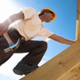 Pracownik w kasku mocuje drewnianą konstrukcję dachu na tle błękitnego nieba. Widoczny młotek przy pasie i robocze rękawice.