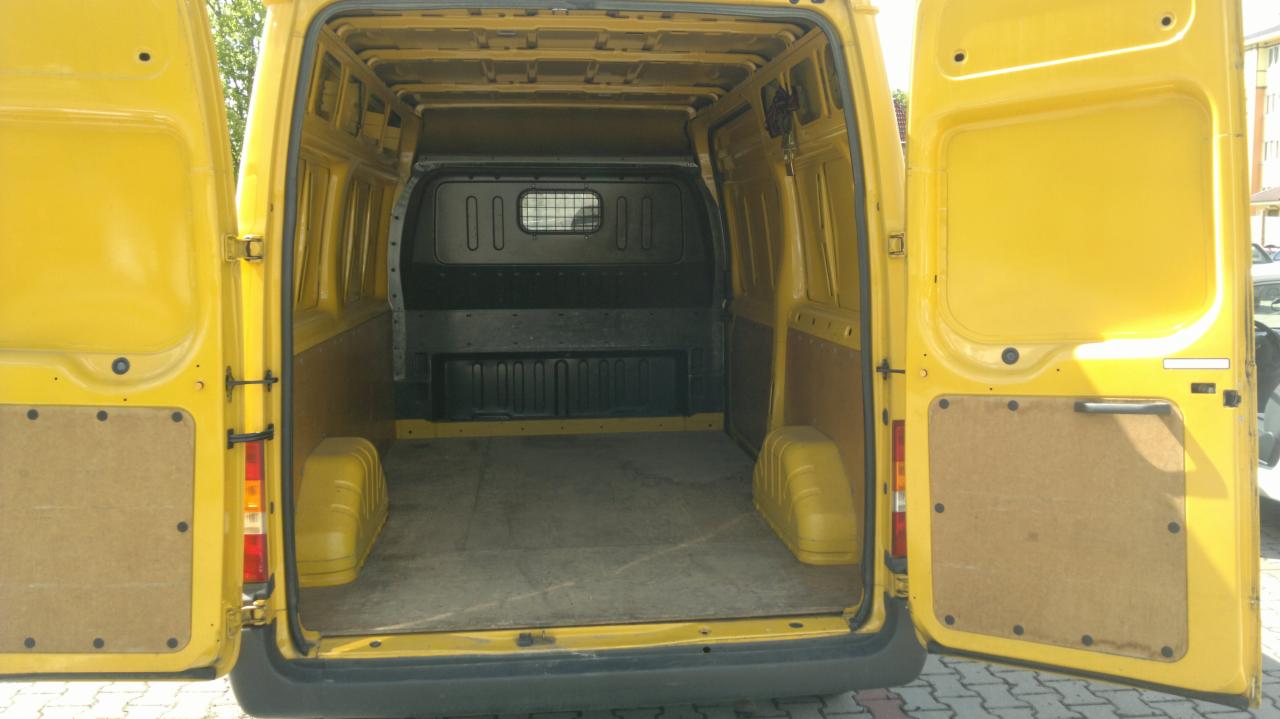 Wnętrze żółtego busa z otwartymi drzwiami, pusta przestrzeń ładunkowa, widoczne elementy wykończenia i oświetlenie. Gotowy do transportu.