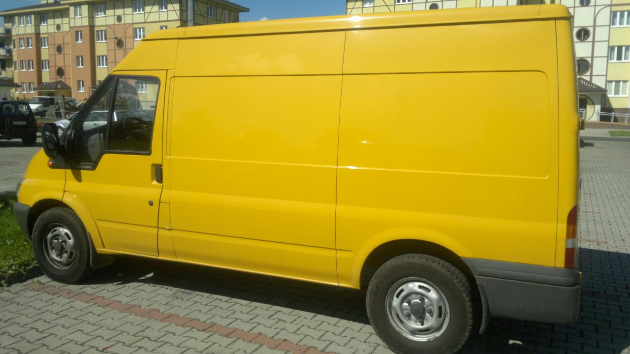 Żółty samochód dostawczy Ford Transit na tle budynku mieszkalnego. Widok z boku, oświetlenie dzienne.
