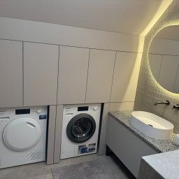 MG MEBLE MICHAŁ GRYT - Szara zabudowa meblowa w łazience z pralką i suszarką Miele, owalna umywalka nablatowa na blacie z szarego granitu, okrągłe lustro z podświetleniem LED.