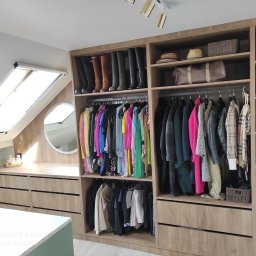 MG MEBLE MICHAŁ GRYT - Jasna garderoba na poddaszu ze skośnym oknem, zorganizowana przestrzeń z butami, ubraniami i akcesoriami na półkach i wieszakach, uzupełniona toaletką z okrągłym lustrem.