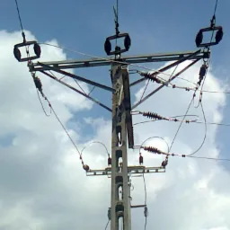 Słup wysokiego napięcia z przewodami na tle pochmurnego nieba. Widok z dołu, ukazujący konstrukcję słupa i izolatory.