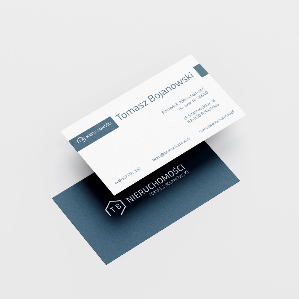 Dwie wizytówki firmy nieruchomości Tomasz Bojanowski, jedna biała z danymi kontaktowymi, druga granatowa z logo i imieniem, leżące ukośnie na jasnym tle.