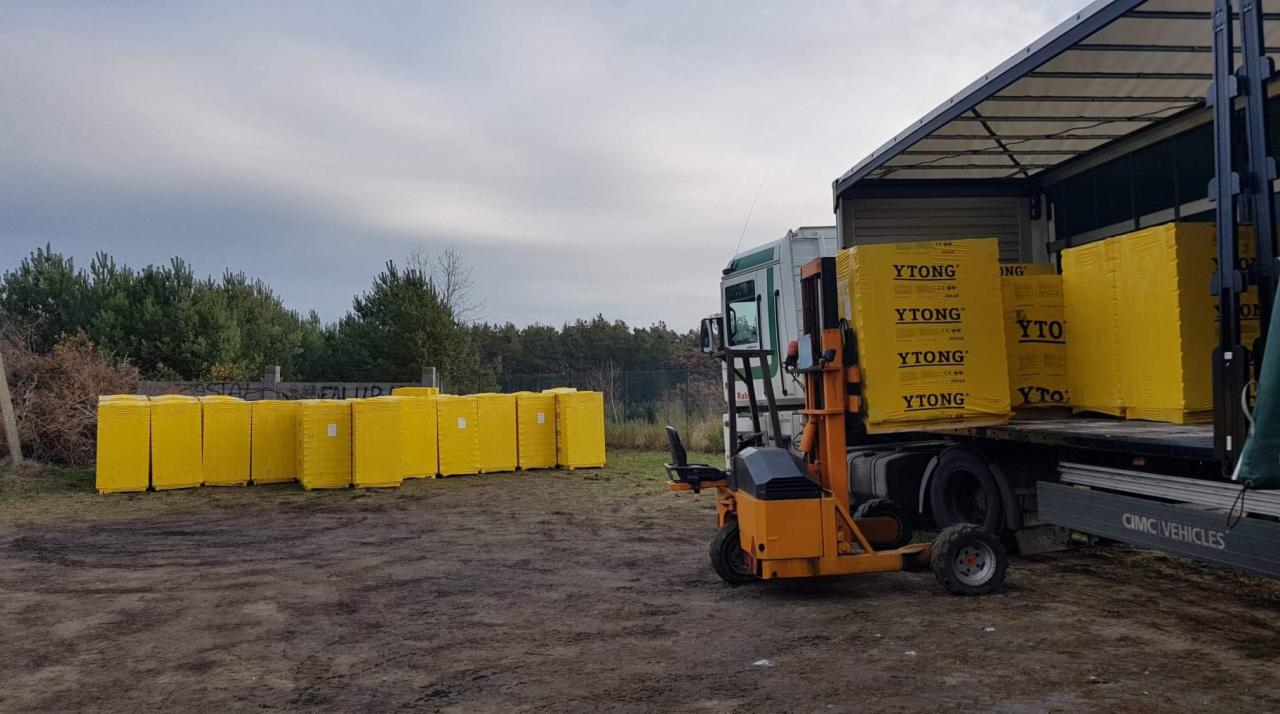 Wózek widłowy załadowuje palety z żółtymi bloczkami Ytong na naczepę ciężarówki na placu budowy.