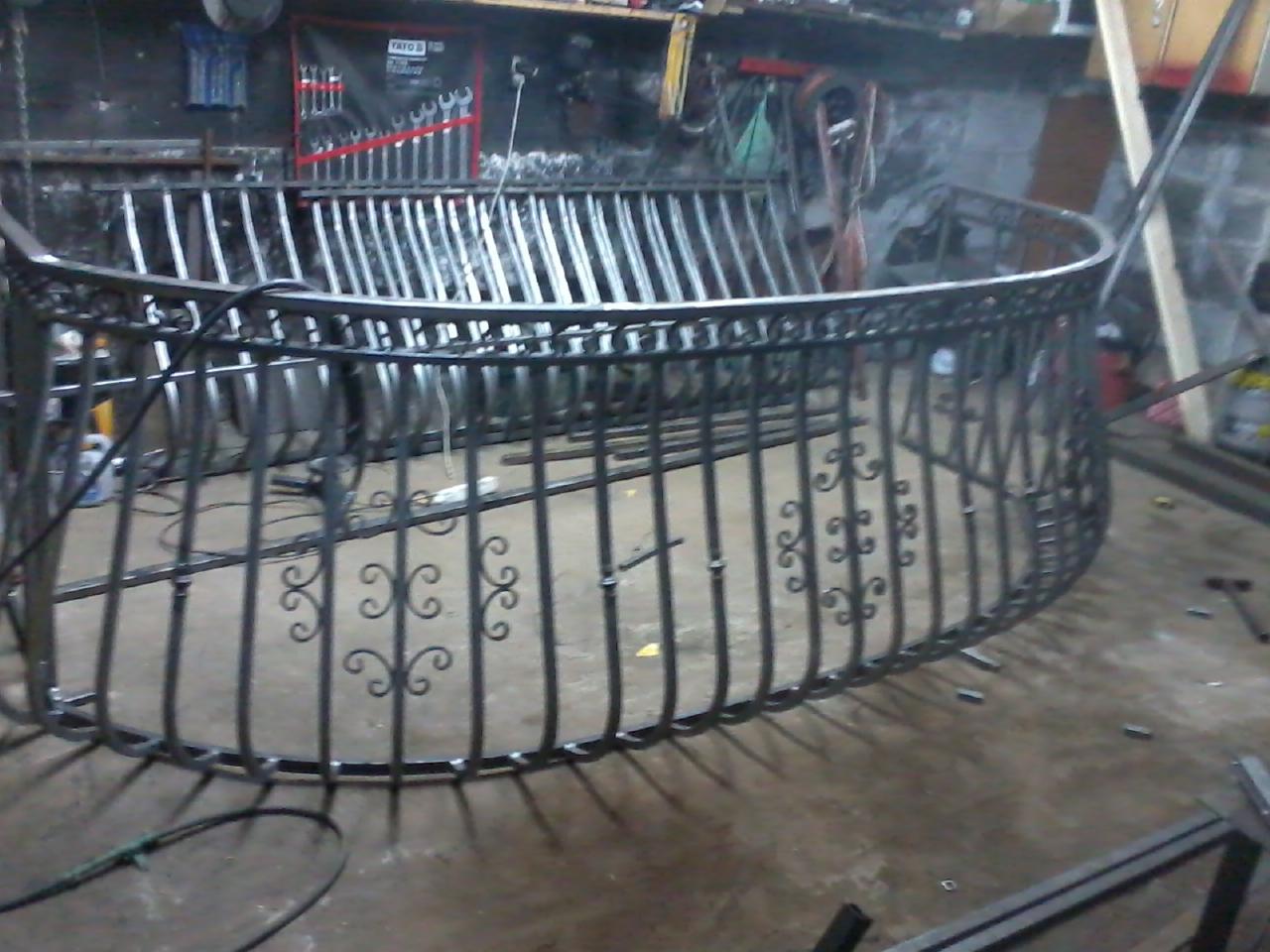 Metalowa balustrada balkonowa z dekoracyjnymi elementami w warsztacie, widoczne narzędzia i akcesoria. Surowy, industrialny klimat. Detal wykonania i spawania.