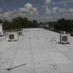 Biały dach płaski z klimatyzatorami i narzędziem. Widok z góry na pokrycie dachowe z elementami montażowymi i sprzętem w słoneczny dzień.