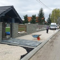 Vagserwis - Układanie kostki brukowej w Dobryszycach, widoczny fragment podjazdu z ułożoną kostką, żwirem i pracownikami w tle. W tle zaparkowane busy.