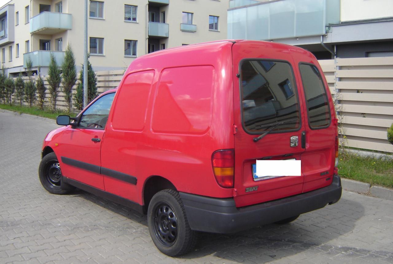 Czerwony Seat Inca, widok z tyłu, zaparkowany na kostce brukowej. Budynek mieszkalny w tle. Pojazd dostawczy z zabudowaną przestrzenią ładunkową.