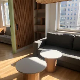 Jasne wnętrze salonu z szarą sofą, dwoma okrągłymi stolikami z marmurowymi blatami i drewnianymi nogami, drewnianą ścianką działową z lamelami oraz wiklinowymi lampami wiszącymi