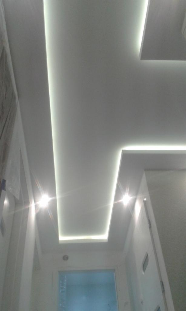 Nowoczesny sufit podwieszany z oświetleniem LED w kształcie prostokątów. Białe ściany i drzwi. Widok z dołu.