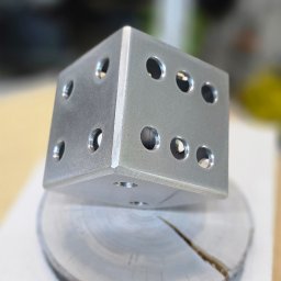 Usługi Spawalnicze Jarosław Kwiecień - Metalowy sześcian z otworami, przypominający kostkę do gry, umieszczony na okrągłej, metalowej podstawie z widocznym pęknięciem.