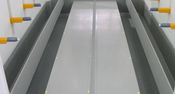 Wnętrze lakierni proszkowej z dyszami natryskowymi na ścianach i pomalowanymi na szaro elementami wewnątrz komory.