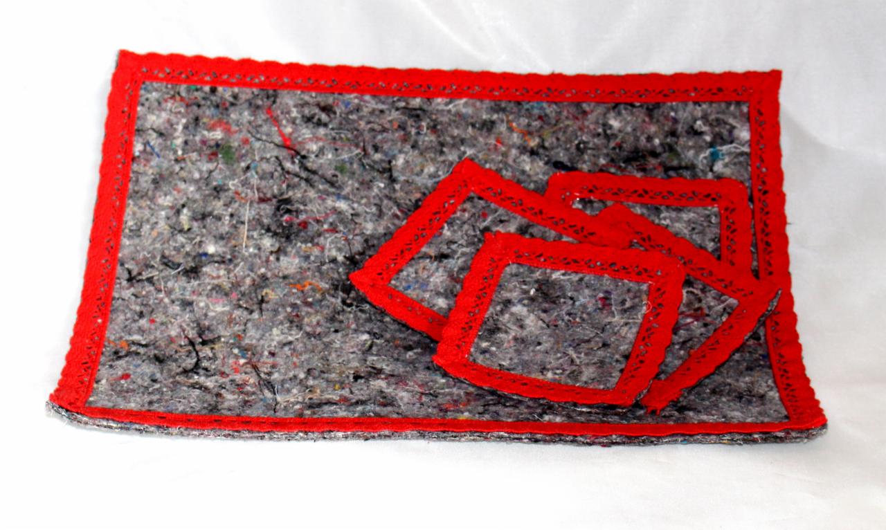 Ręcznie wykonana mata z szarego filcu z czerwoną, dzierganą obwódką i trzema czerwonymi, dzierganymi kwadratami, leżąca na białym tle.
